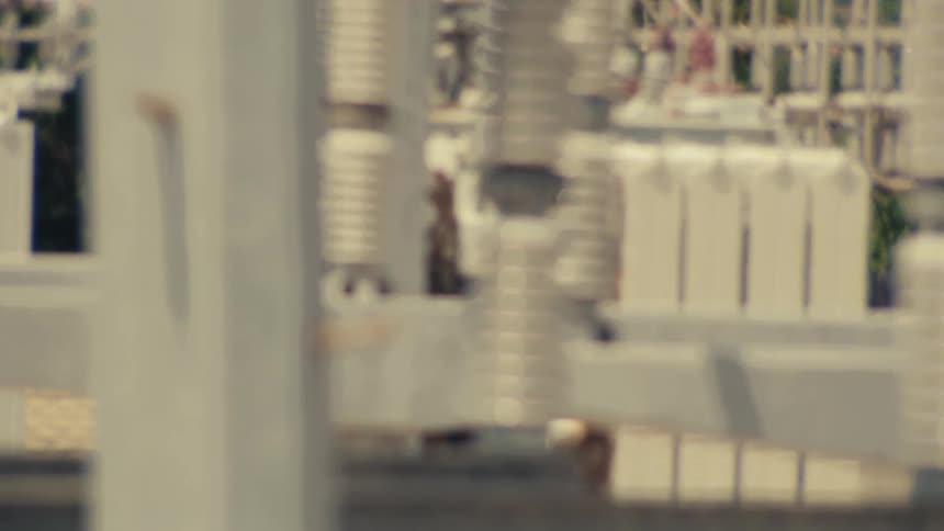 A detailed view of a high-voltage electrical power substation with a slow camera pan across insulators and conductors on a hot day