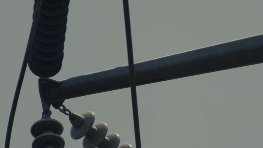 A detailed close-up shot pans along high-voltage electrical insulators and power lines on a transmission tower