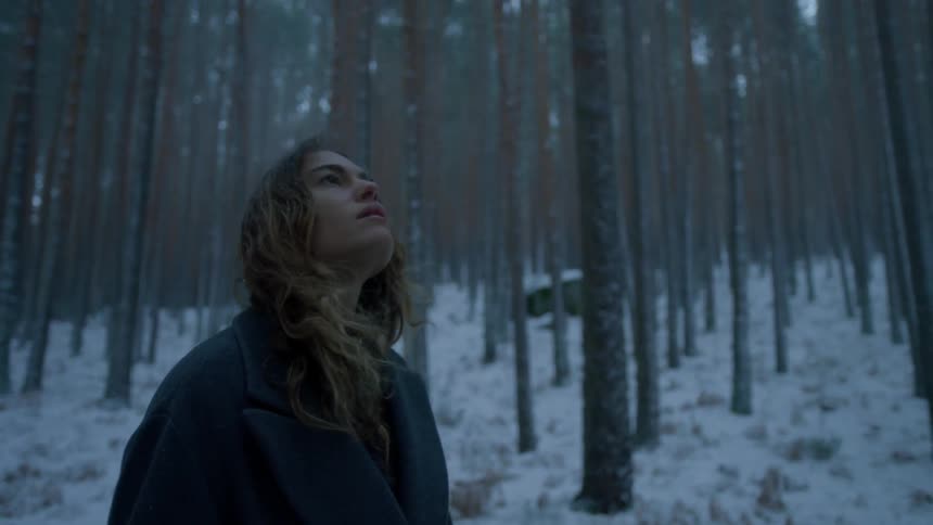Woman looks up while standing in snowy woods