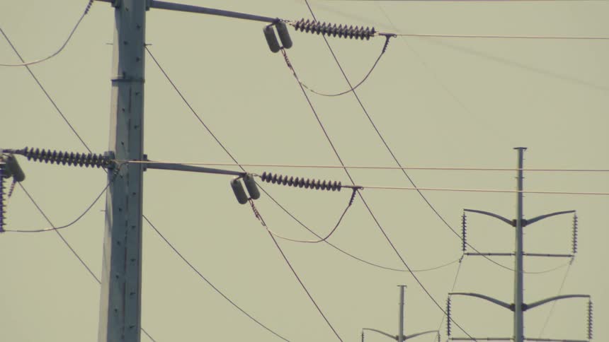 A slow upward tilt reveals the details of a large electrical transmission tower and its power lines against a hazy sky