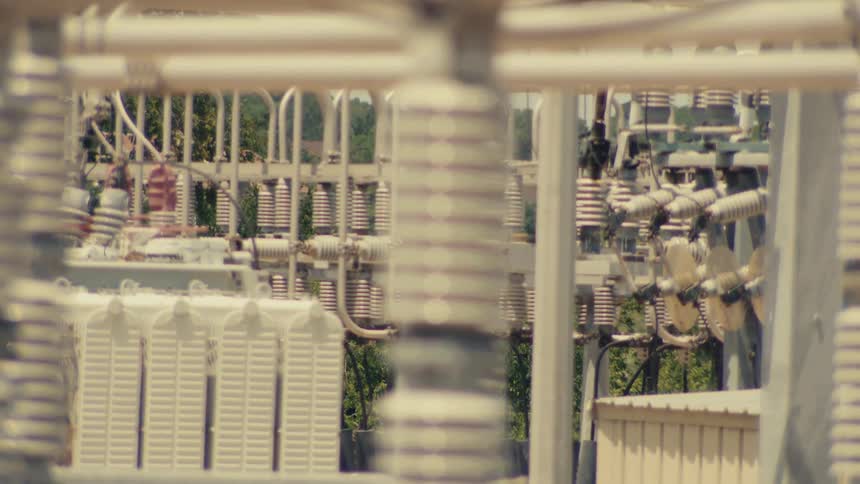 A slow rack focus shot of a ceramic insulator at a high-voltage electrical power substation on a hot day