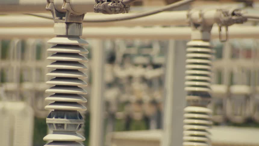 A close-up view of a high-voltage electrical substation with a slow pan and tilt across the insulators and power lines