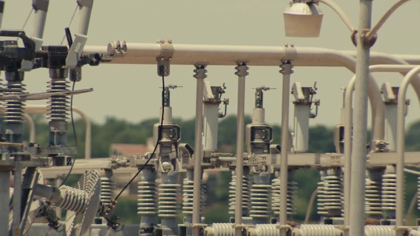 A detailed pan shot of an industrial electrical power substation with transformers, insulators, and conductors on a sunny day