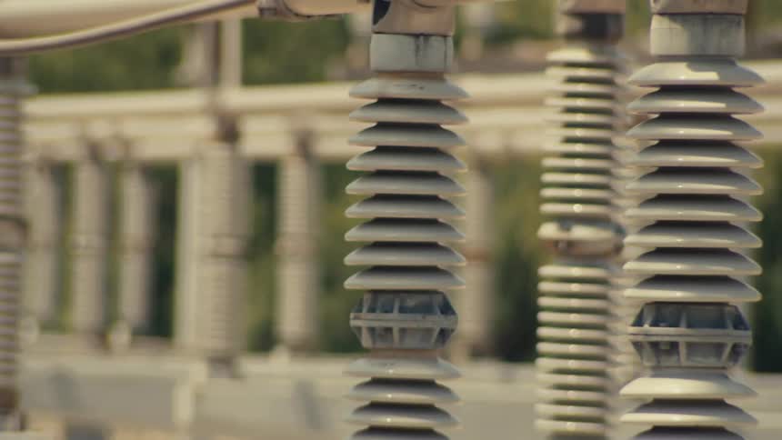 A slow pan across the ceramic insulators and metal structures of a high-voltage electrical power substation