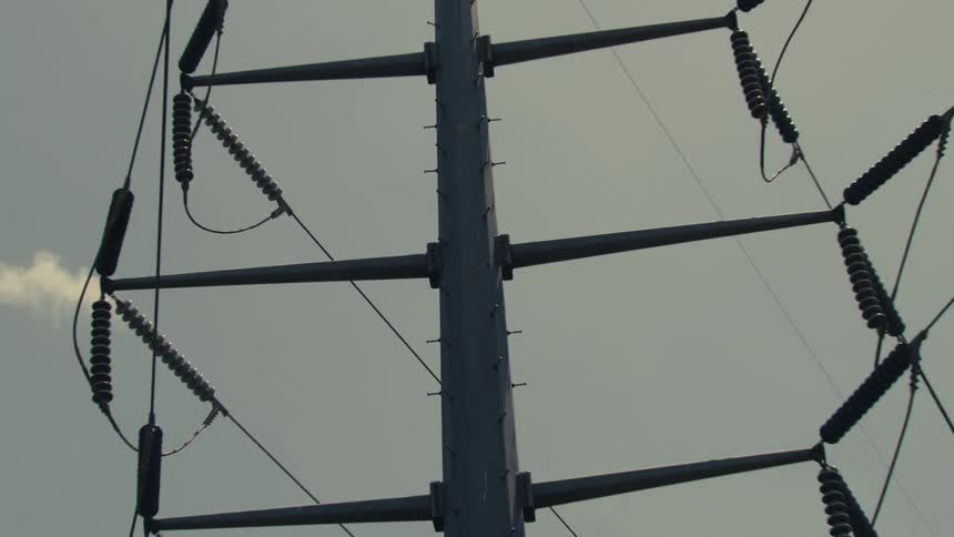 A close-up of a high-voltage power line tower in the rain zooms out to reveal its full structure against an overcast sky