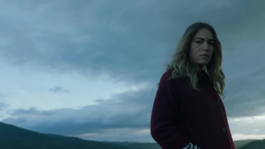 A woman stands in thought outside overlooking a valley