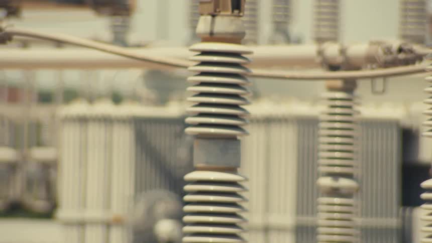 A detailed close-up pan across ceramic electrical insulators and infrastructure at a power plant substation