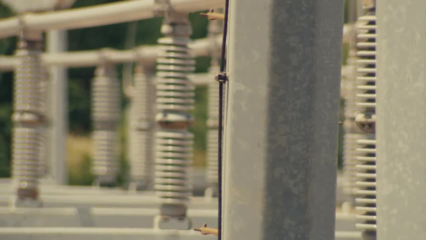 Slow sliding shot across rows of ceramic insulators at an industrial electrical power substation on a sunny day