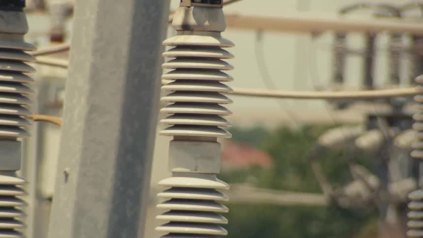 A slow revealing pan of the intricate machinery and insulators at an electrical power substation on a bright day
