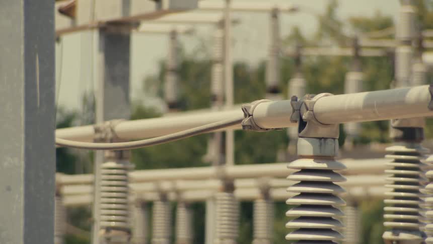 A slow, cinematic tilt-down shot reveals the intricate components and insulators of a high-voltage electrical substation