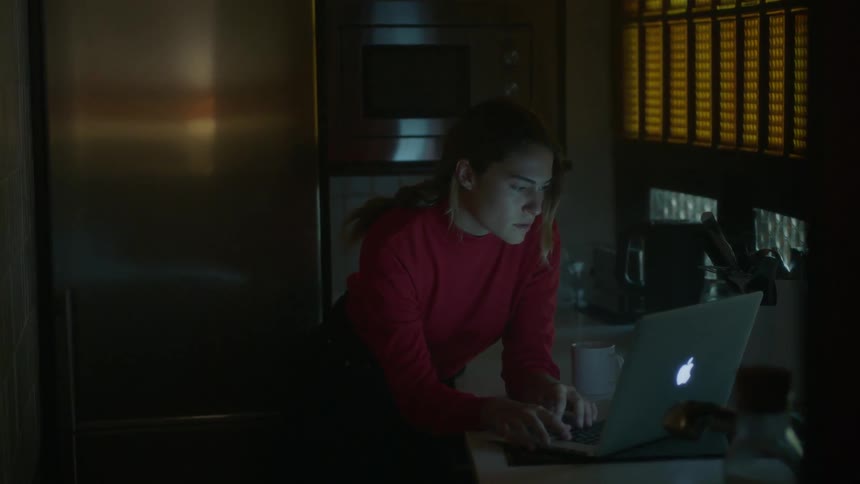 Woman closes a laptop in a dim room