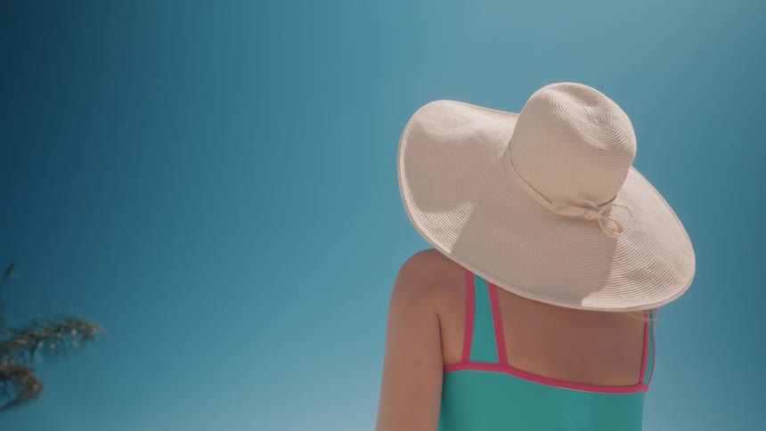 A woman in a stylish swimsuit and wide-brimmed sun hat enjoys a sunny day against a clear blue sky