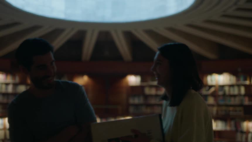 A man and woman joke and laugh while standing in a library