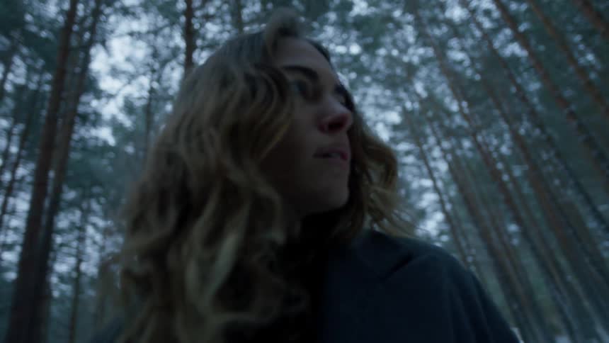 A woman looks up at the tree tops in a forest