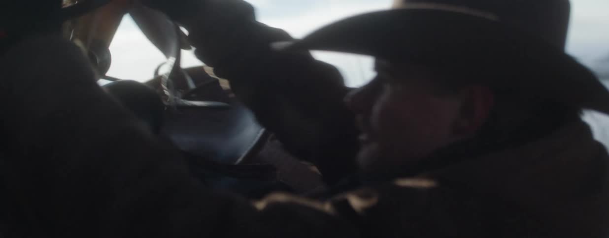 A cowboy adjusts his horse's saddle in slow motion as the sun shines over a snowy landscape