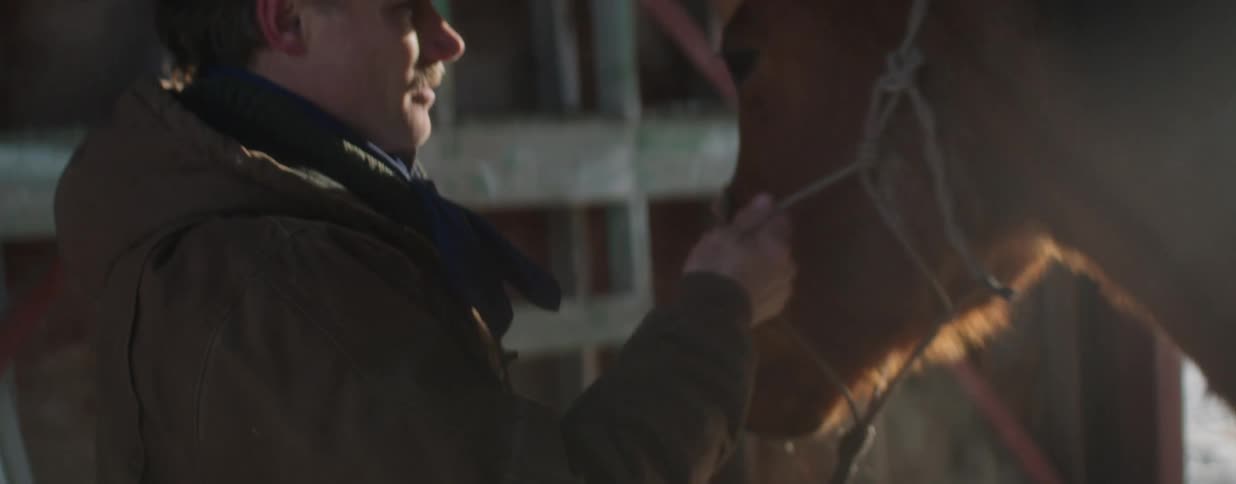 A cowboy tenderly strokes his horse's face in a sun-drenched barn, showing their deep bond in slow motion