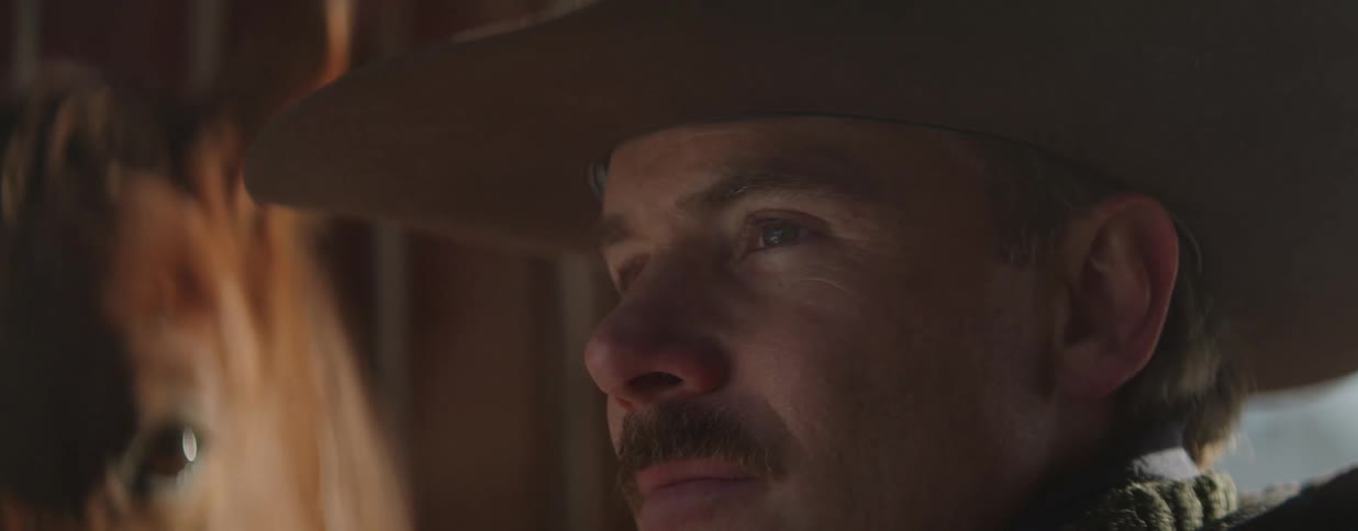 Close up profile of a cowboy with a mustache and hat looking thoughtfully into the distance