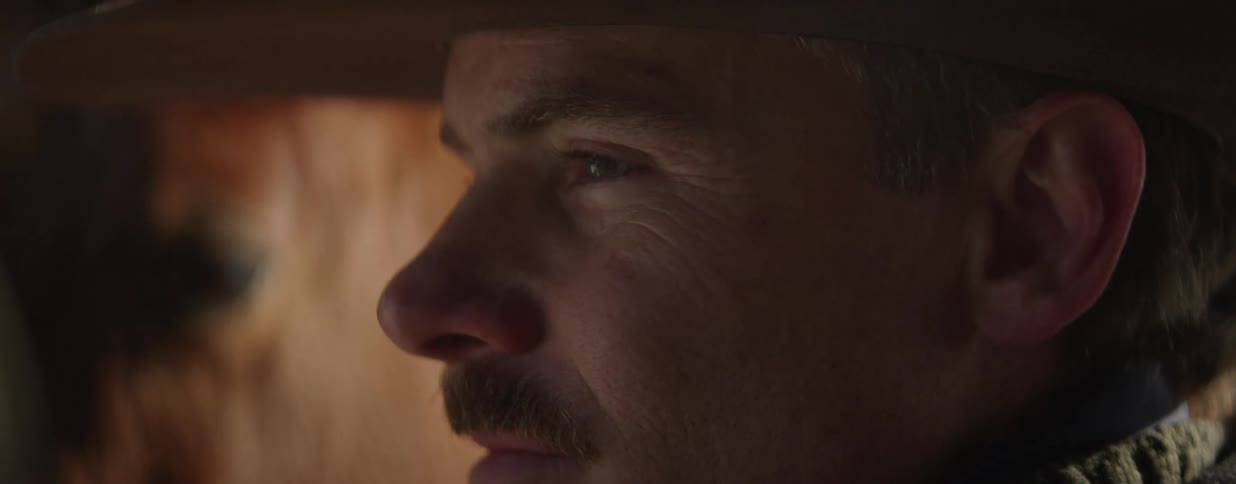 A dramatic extreme close-up profile shot of a serious cowboy with a mustache in dim, warm lighting