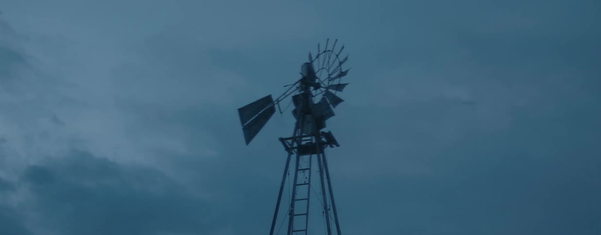 A solitary old-fashioned windmill stands still against a dark, moody sky as evening approaches