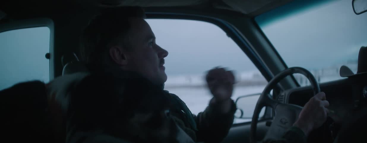 A man with a mustache and his loyal dog companion enjoy a drive through a wintery landscape