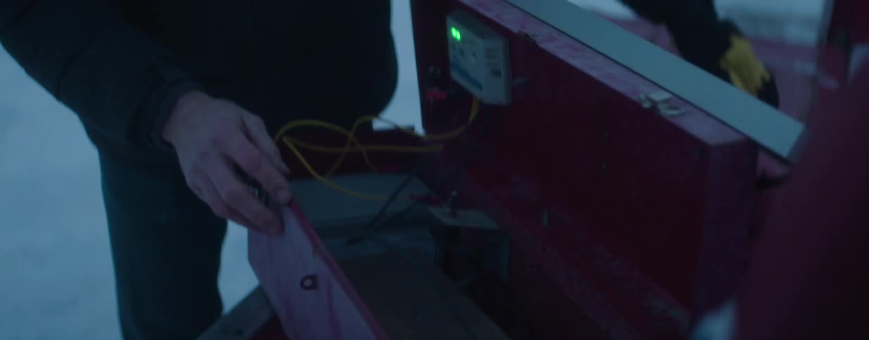 Close-up shot of a man opening a solar panel charging box and working on the electronics in the snow
