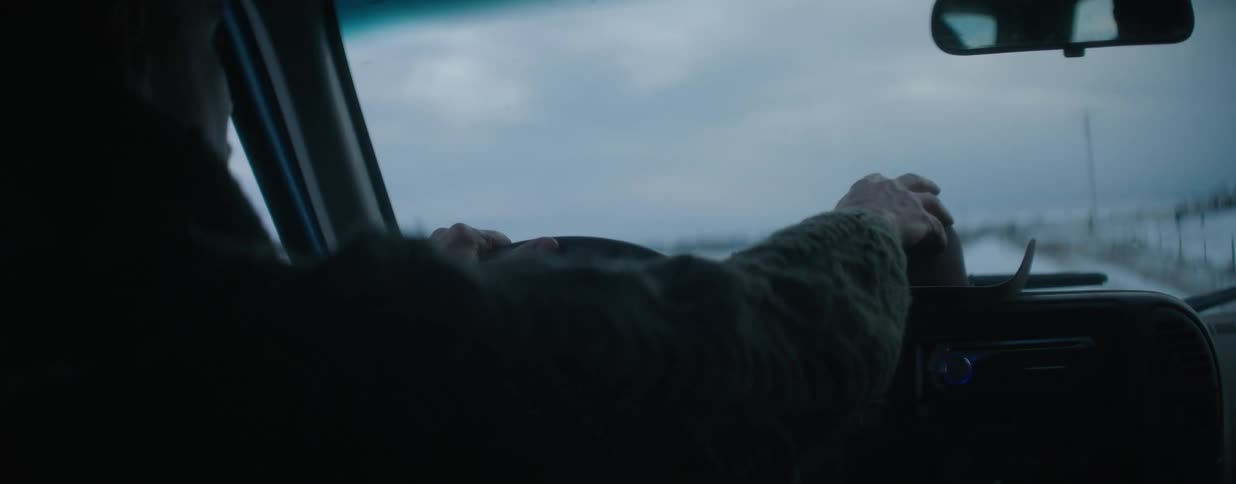 Interior shot of a person driving a truck through a snowy landscape on a cold day with a cowboy hat on the dash