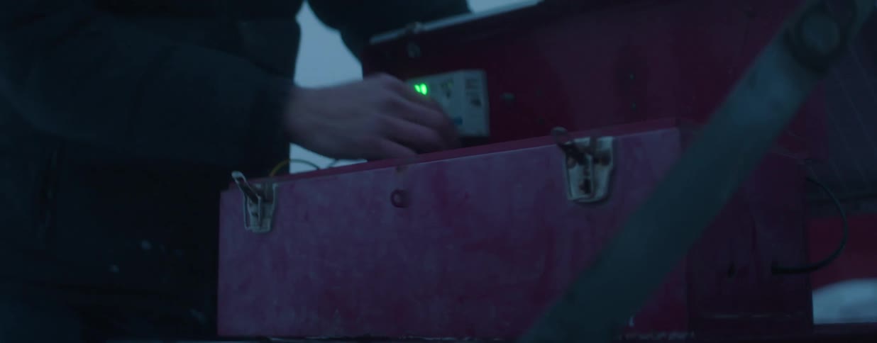 A person opens a solar-powered equipment box and checks the blinking green light on the electronics inside during winter