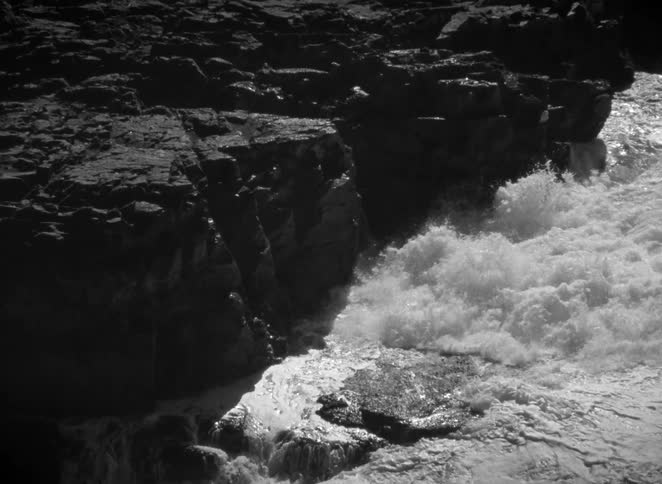 Dramatic black and white footage of a powerful river current crashing against rugged rocks