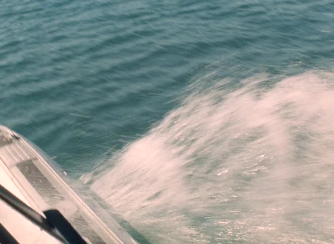 Point-of-view shot from a vintage seaplane speeding across the water, starting with a view of the splashing pontoon and moving into the cockpit