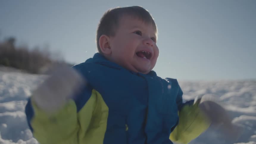 An adorable toddler expresses pure joy, laughing and flapping their arms while playing in the snow under the sun
