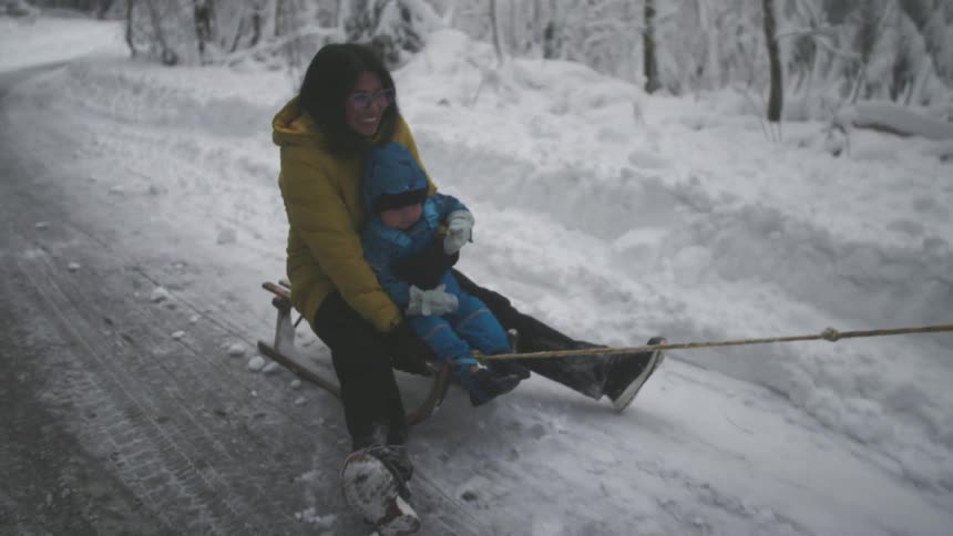 A happy mother and her young son enjoy a slow-motion sled ride through a snowy winter forest