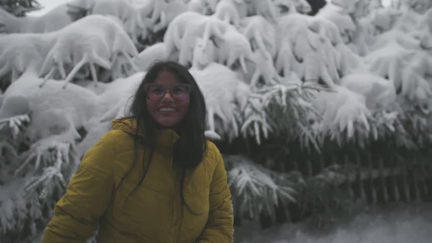 A slow-motion close-up captures the joy of a smiling woman in a yellow jacket standing amidst snow-covered trees