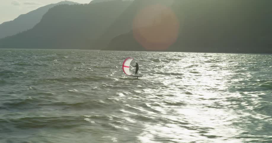 A lone wing foiler glides across a sun-drenched river in slow motion, surrounded by a dramatic mountain gorge