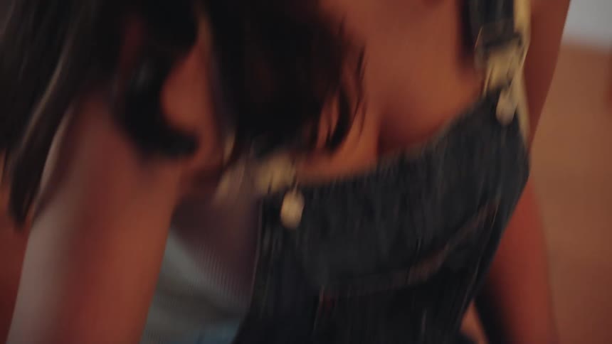 A close-up shot follows an artist's hand as she delicately paints a straight line, then tilts up to reveal her focused expression
