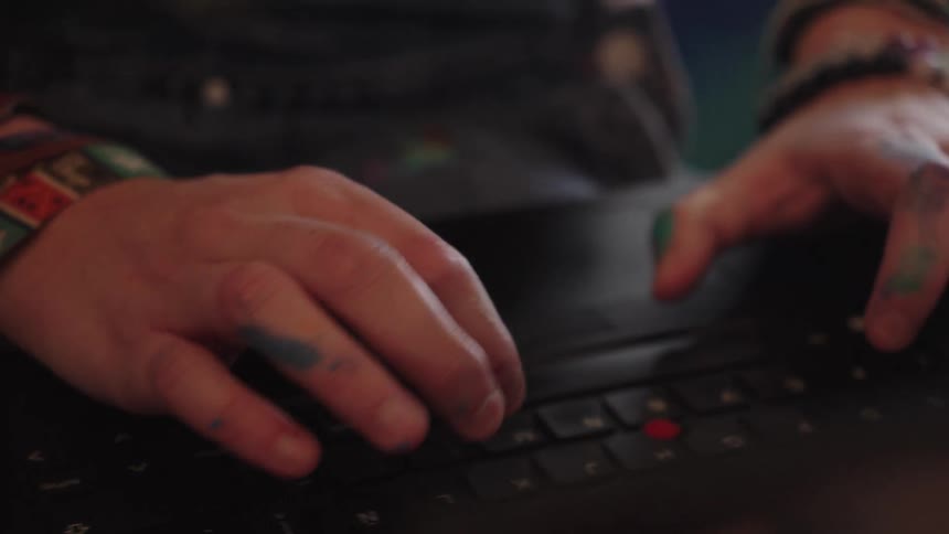 Close-up of an artist's paint-splattered hands typing on a laptop keyboard