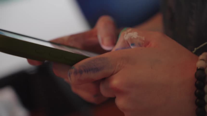 A close-up shot of an artist's paint-stained hands scrolling and typing on a smartphone