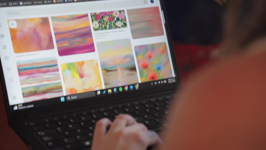 A person browses for colorful, abstract art inspiration on a laptop, with a focus on their hand using the trackpad