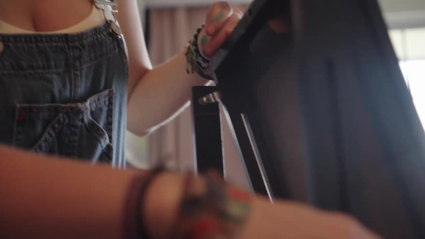 A creative young woman in denim overalls carefully adjusts her easel before starting her artwork