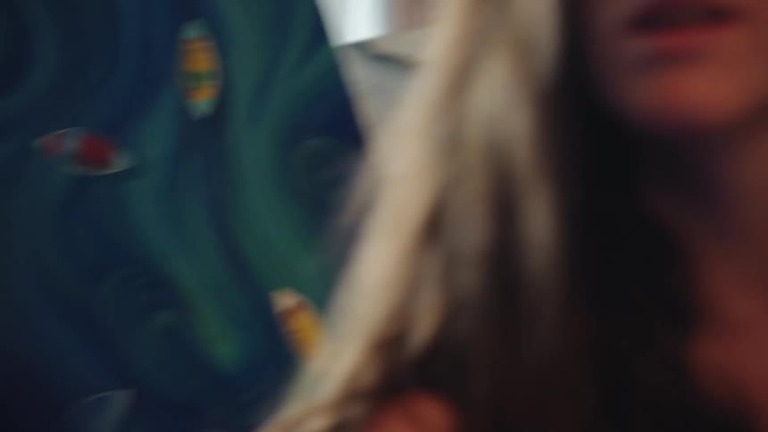 A close up rack focus from an artist's hand holding a paintbrush to her concentrated face