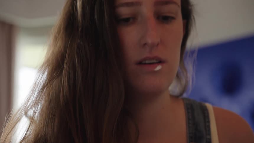 Close-up of a focused young female artist in denim overalls opening a jar of red paint in her studio