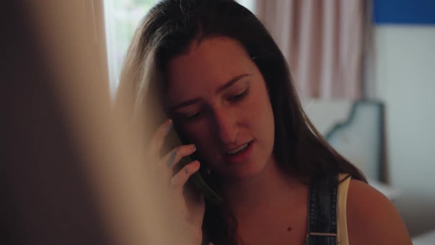 A young female artist with paint on her hand takes a break to talk on her smartphone in her studio
