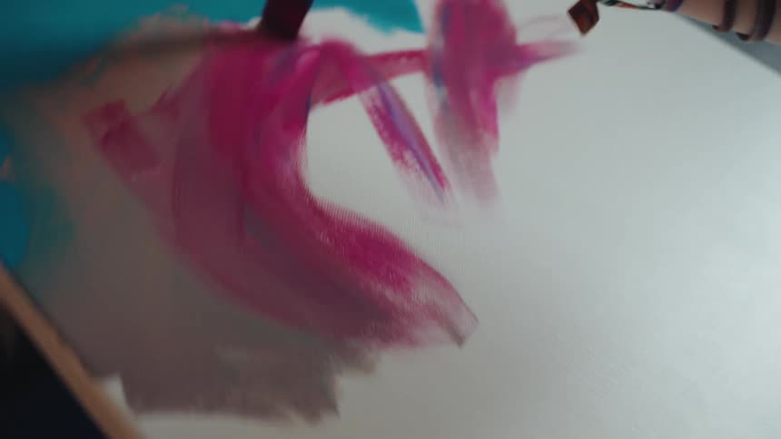 A close-up slow-motion shot shows a young woman artist expressively applying vibrant pink paint to a white canvas