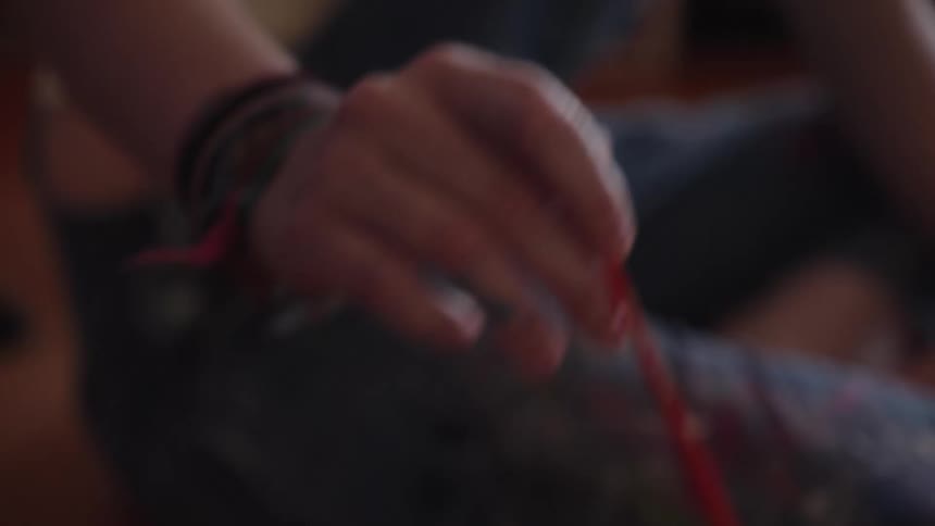 An artist's hand selects a thin red paintbrush from a jar, pulling back to reveal a blue abstract painting of water on a canvas