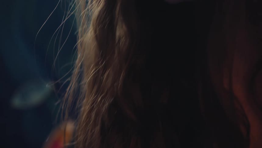 Close-up of a young female artist's hand painting a blue canvas, tilting up to her focused face in profile