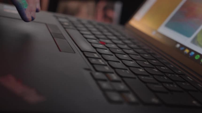 An artist with paint on their hands uses a laptop trackpad to browse colorful, inspirational images online