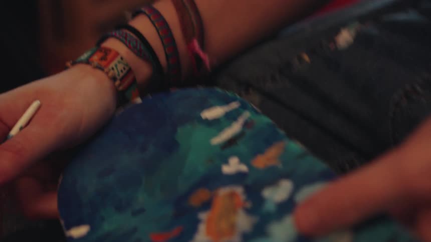 Slow-motion close-up of an artist's hands carefully painting an abstract design on a skateboard deck in their studio