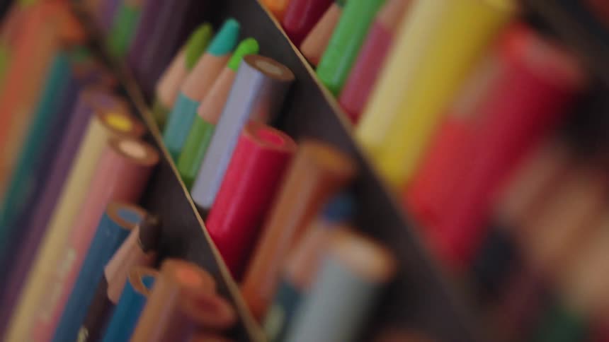 A dreamy, shallow depth-of-field close-up shot slowly pans across a vibrant set of colored pencils in a box