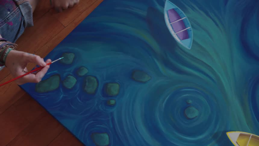A high-angle view of an artist carefully painting details on a large canvas of colorful boats floating in swirling blue water