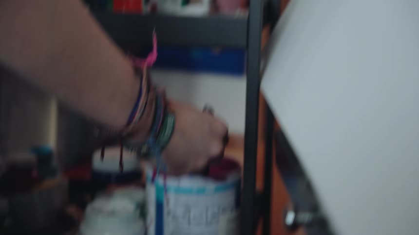 A close-up shot of a bohemian-style artist painting vibrant magenta strokes on a canvas in their cluttered studio