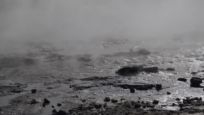 Steam rises from bubbling geothermal hot springs in a misty, rocky landscape